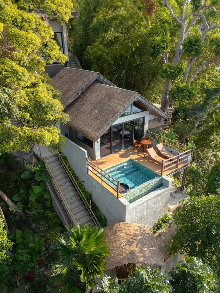 Aerial view of a private pool villa and sun deck nestled in lush tropical greenery