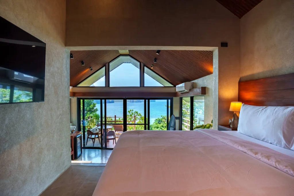 Main Villa king bed beneath a vaulted ceiling with panoramic windows beyond