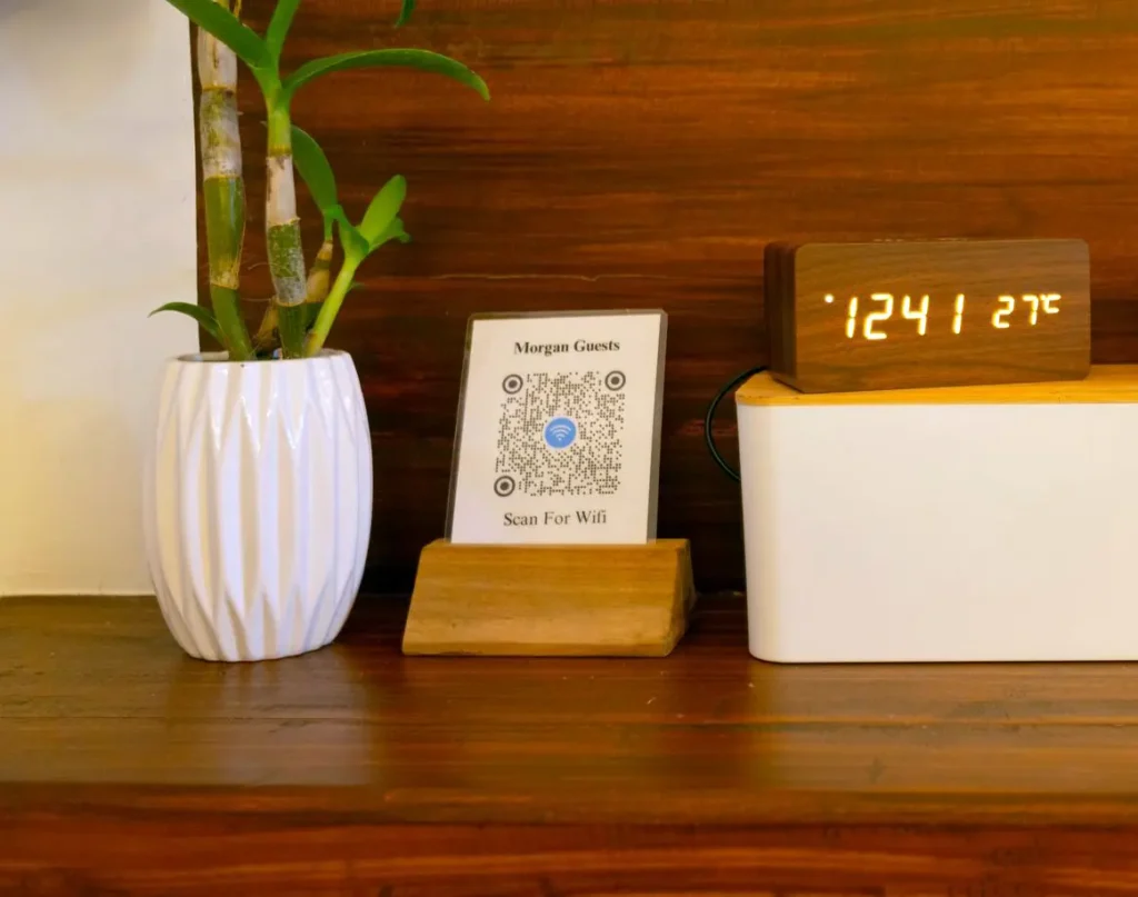 Guest Wi-Fi QR code, digital clock, and plant on a wooden shelf at Morgan Villas